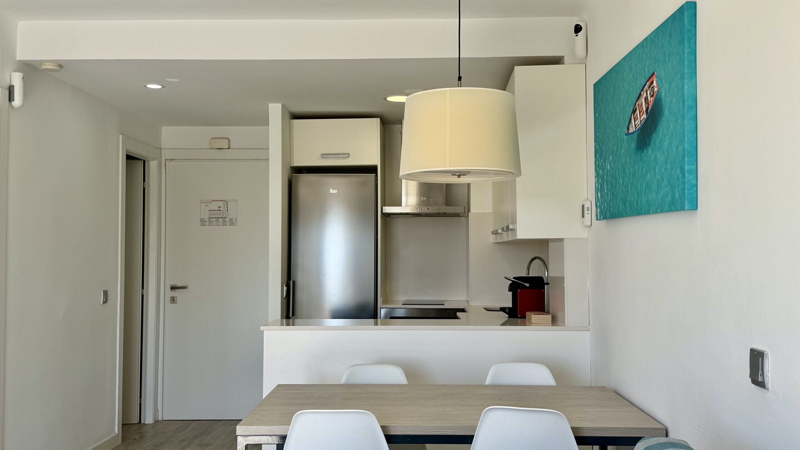 A modern kitchen with a built-in refrigerator, a hanging light fixture, and a dining area with a table and chairs.