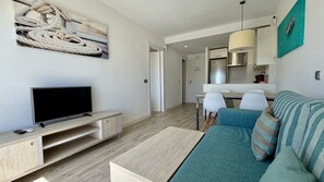 Ein modernes Wohnzimmer mit Flachbildfernseher, einer Couch, einem Couchtisch und einem Essbereich mit Stühlen.