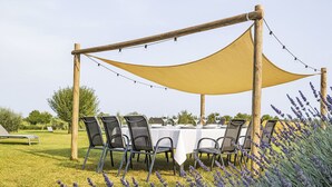 Un área de comedor al aire libre con una mesa dispuesta para seis personas, rodeada de sillas, bajo un toldo.