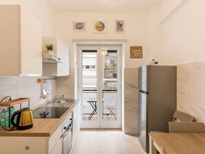 Une cuisine compacte équipée d’un réfrigérateur, d’une cuisinière et d’un évier. Des tableaux encadrés ornent le mur et une petite plante est posée sur le comptoir.