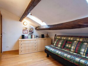 Ein gemütliches Zimmer mit Holzbalkendecke, einem Karomuster-Sofa, einem Holzschrank und einem kleinen Tisch mit verschiedenen Gegenständen.