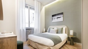 Un dormitorio moderno con cama, mesitas de noche, una ventana con cortinas, un radiador y un cuadro colgado en la pared.
