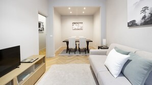 Una sala moderna con un televisor de pantalla plana, un sofá, una mesa de comedor con sillas y un cuadro en la pared.