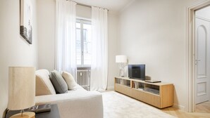 Una sala de estar moderna con un sofá, un televisor sobre un mueble de madera, una lámpara y una ventana con cortinas.