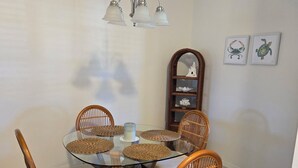 A dining area with a round glass table, wicker chairs, a hanging light fixture, and wall-mounted shelves with decorative items. - Cozy 2-bedroom condo in nice Fort Myers (Fort Myers)