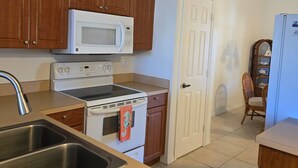 A kitchen with wooden cabinets, a white microwave, a stove, and a sink. - Cozy 2-bedroom condo in nice Fort Myers (Fort Myers)