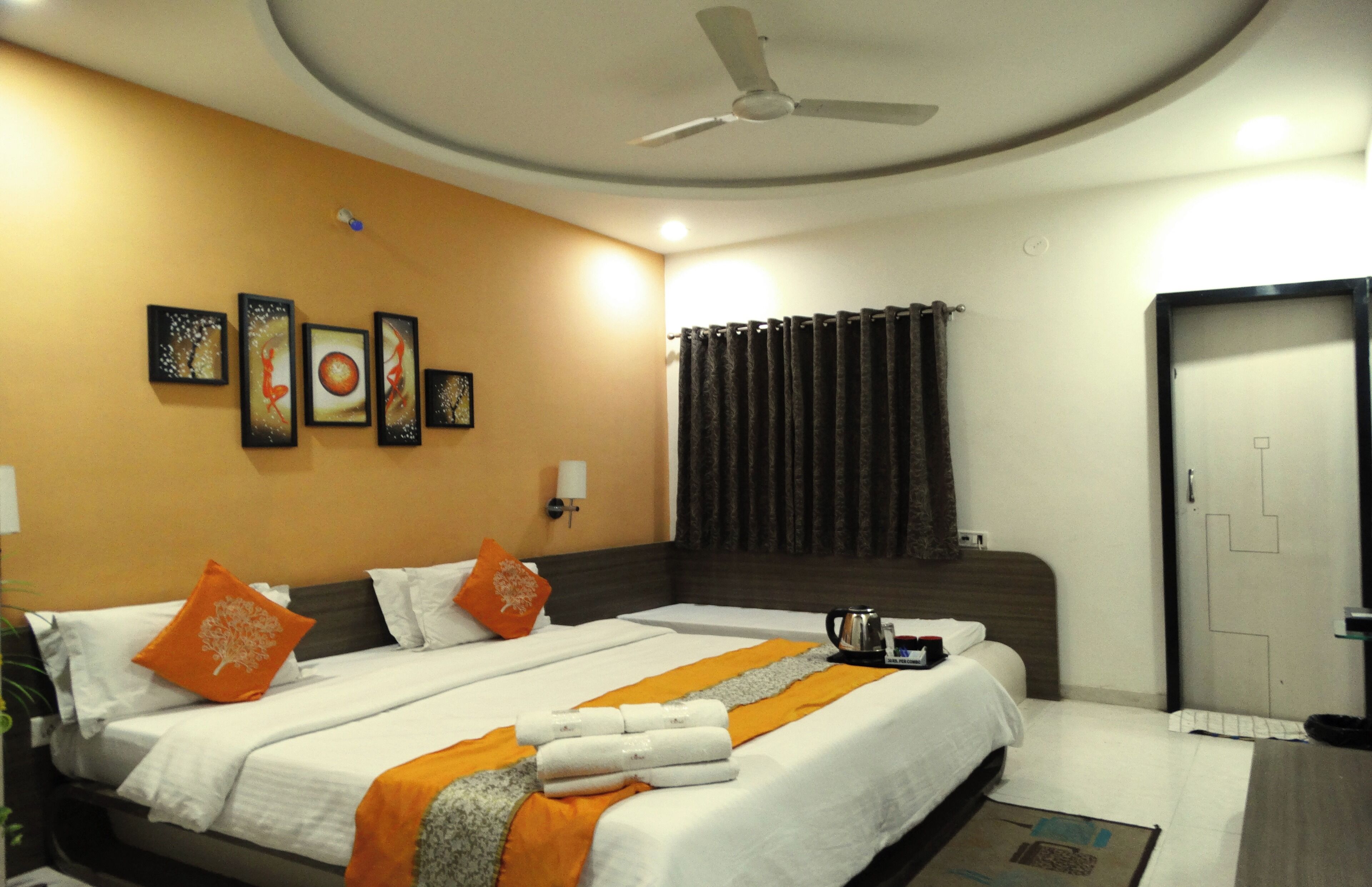 A hotel room with two beds, a ceiling fan, artwork on the wall, and a door.