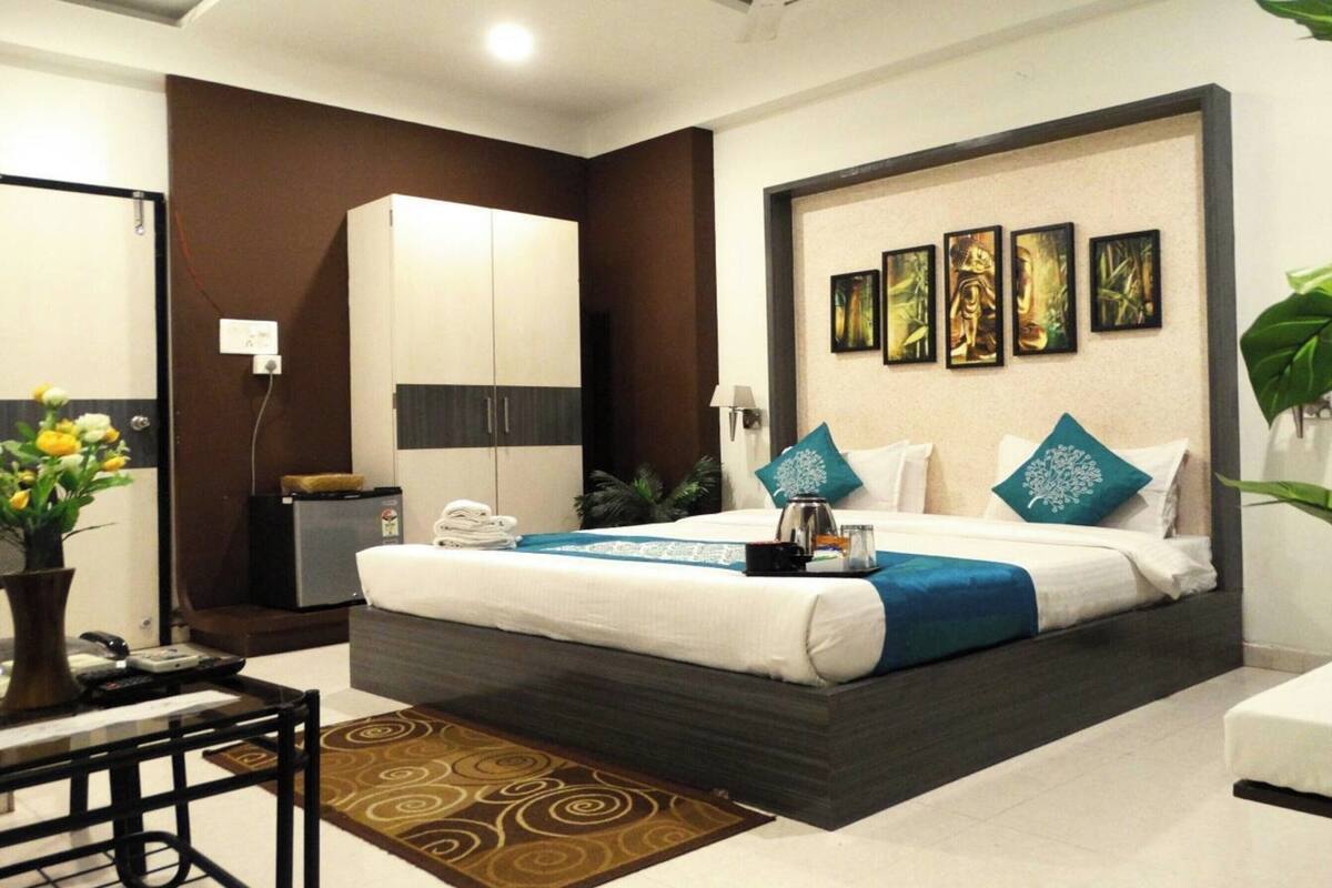 A modern hotel room with a bed, a desk, a wardrobe, and a wall with framed artwork.