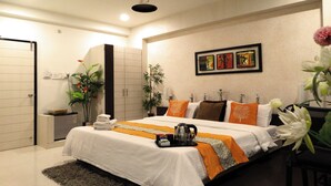 Une chambre d’hôtel moderne avec un grand lit, un ventilateur de plafond, des œuvres d’art accrochées au mur et une plante en pot.