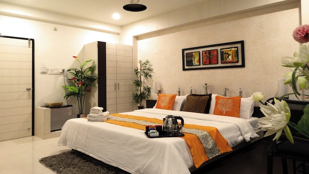 A modern hotel room with a large bed, a ceiling fan, artwork on the wall, and a potted plant. - Hotel Crown (Rajkot)