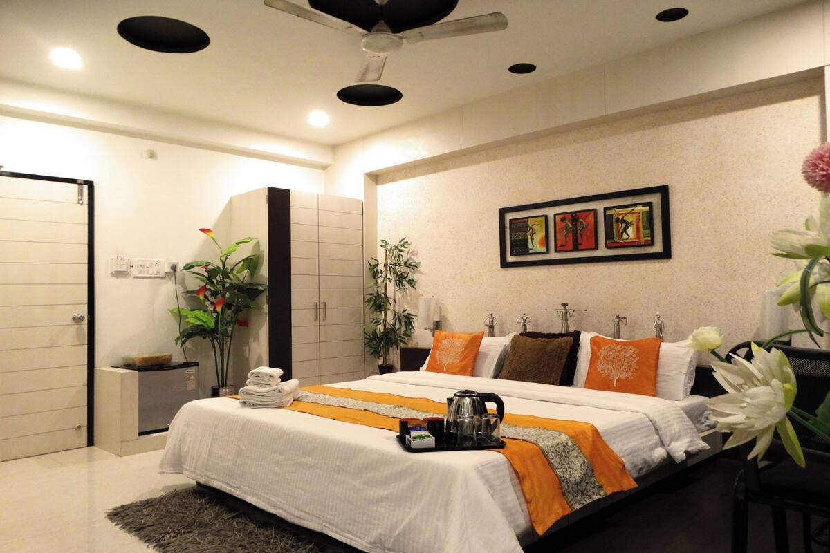 A modern hotel room with a large bed, a ceiling fan, artwork on the wall, and a potted plant.