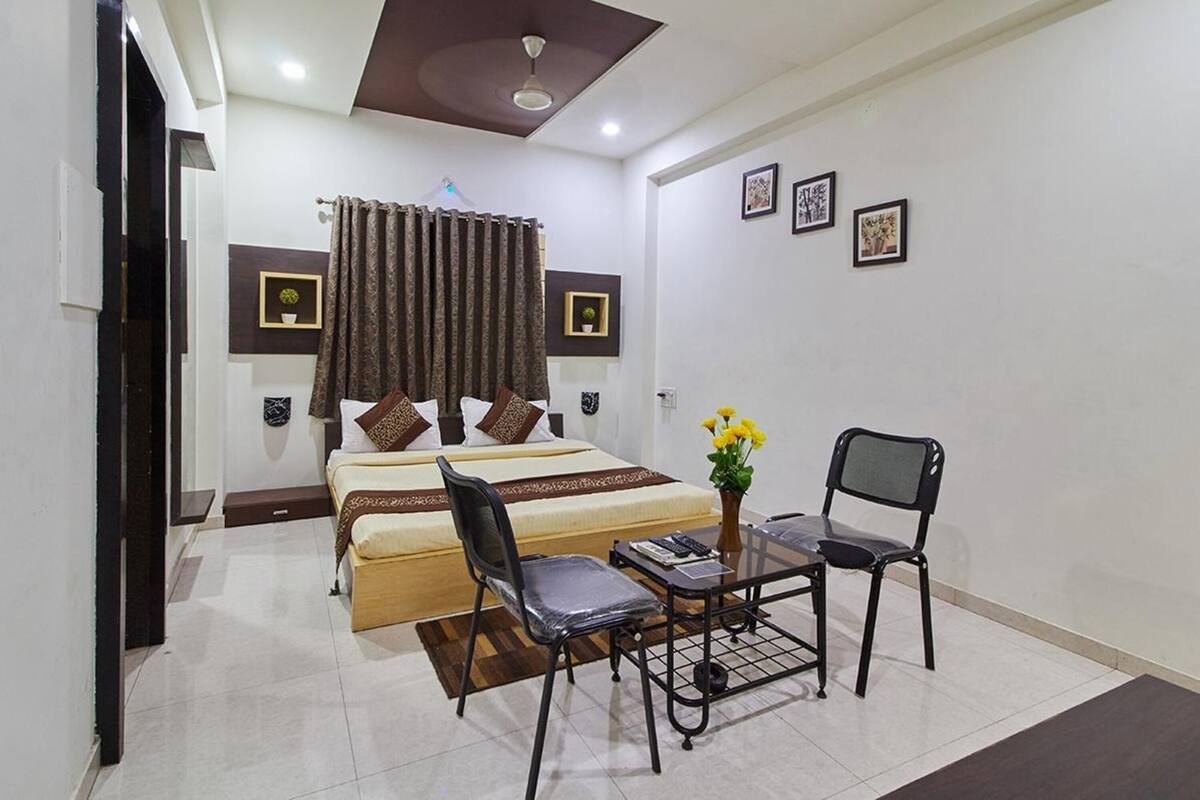 A bedroom with a bed, two chairs, a small table, a ceiling fan, and wall-mounted artwork.