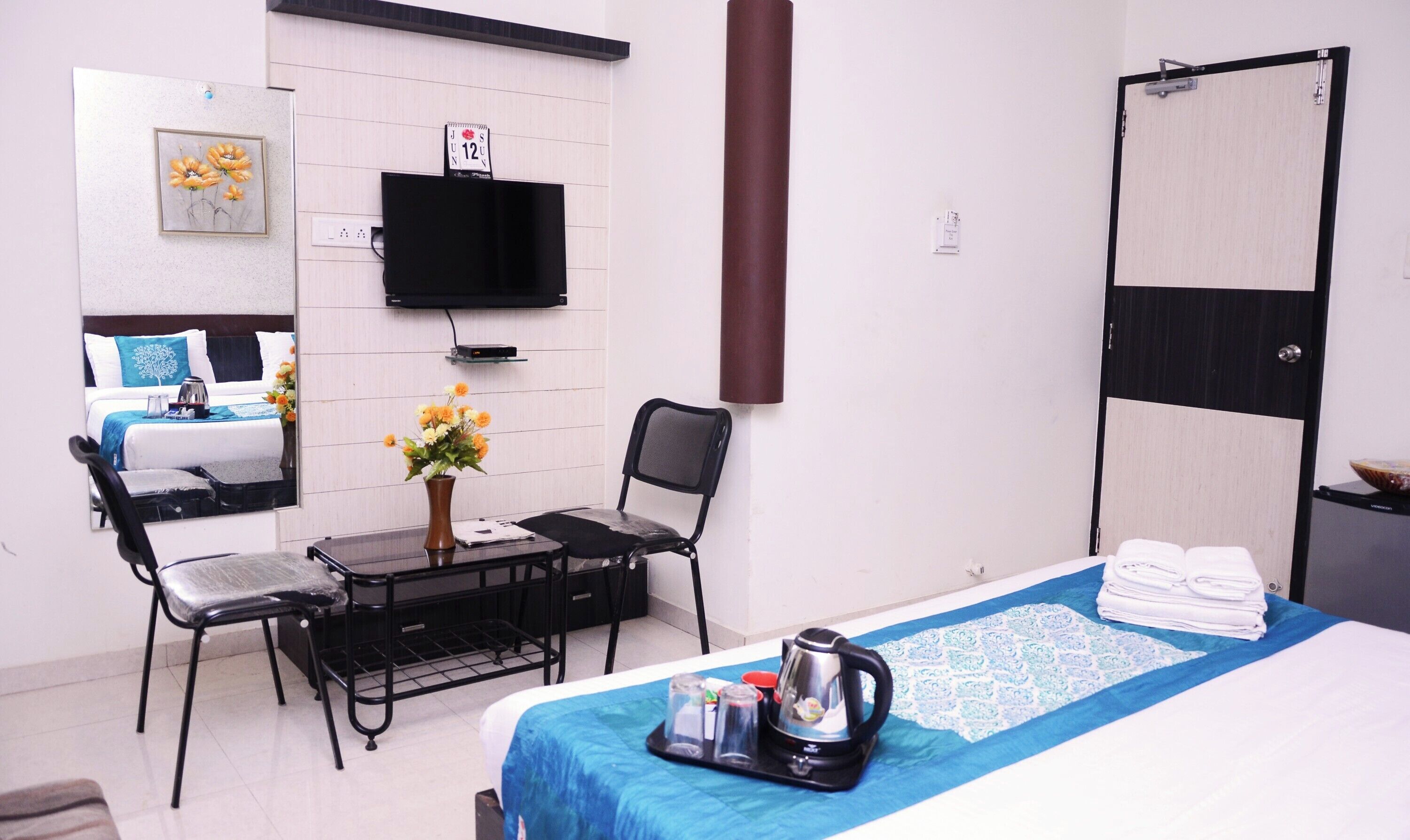 Une chambre d’hôtel comprenant un lit, un bureau avec une chaise, une télévision, une armoire et une petite table avec une bouilloire et des tasses.