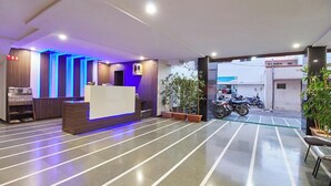 A reception area with a reception desk, potted plants, and a view of parked motorcycles outside. - Hotel Crown (Rajkot)