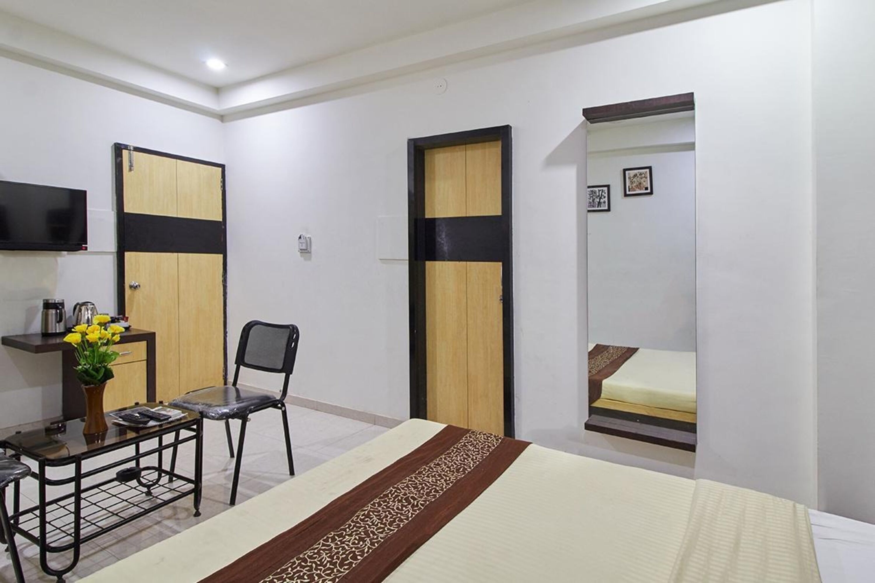 A hotel room with a bed, a desk with a chair, a TV, and two doors.