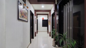 A hallway with a framed artwork on the left, a potted plant on the right, and a door at the end. - Hotel Crown (Rajkot)