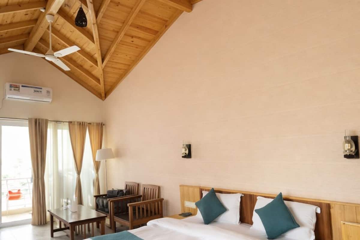Une chambre avec un grand lit, des poutres apparentes en bois au plafond, des ventilateurs de plafond, un bureau et une chaise.