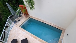 Una pequeña piscina al aire libre con dos sillas de descanso, una mesa y una planta en maceta.