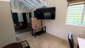 Una sala de estar con televisor de pantalla plana, ventilador de techo, ventana con persianas y sofá con cojín.