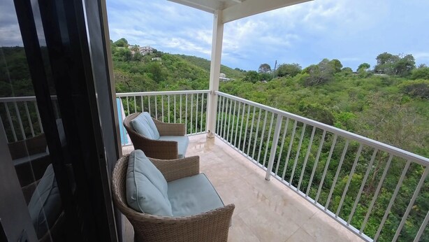 Un balcón con mobiliario de mimbre y vistas a un paisaje verde exuberante.