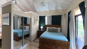 Un dormitorio con cama, espejo, mesita de noche, ventilador de techo y ventana con cortinas.