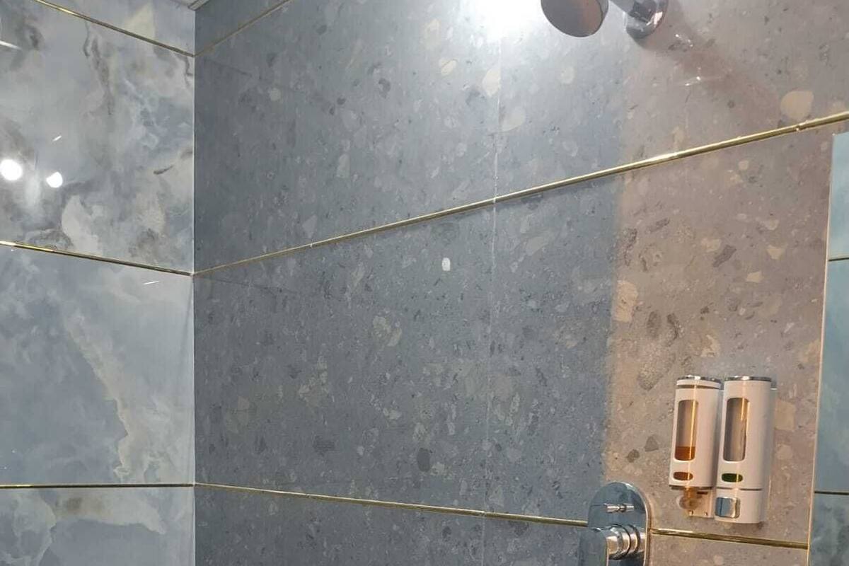 Een badkamer met een marmeren wand, een toilet, een wastafel en een douche met een glazen deur.