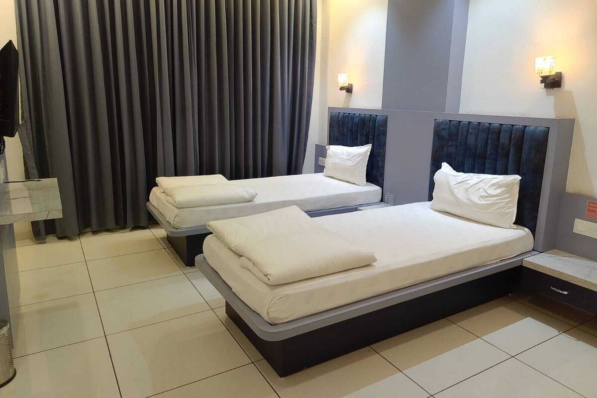 Een hotelkamer met twee bedden, een groot raam met gordijnen, een nachtkastje en een wandlamp.