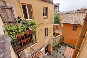 A narrow urban street with buildings, a balcony with potted plants, and a traditional tiled roof. - Lovely Trastevere Loft (Rome)