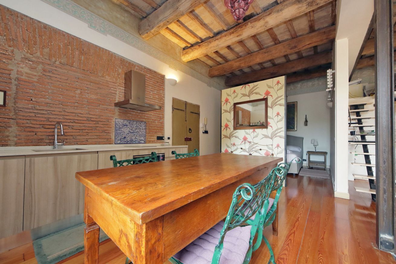 Een keuken met een houten tafel, groene stoelen, een bakstenen muur en een houten plafond.