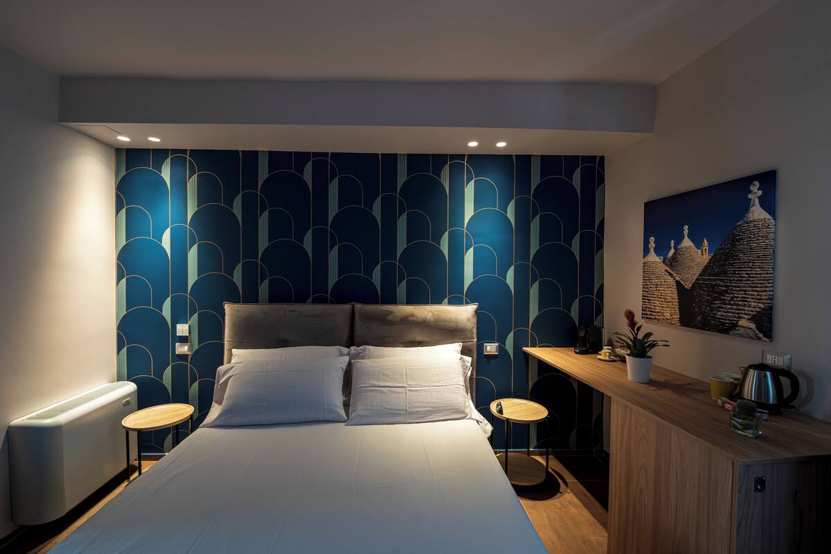 A bedroom with a bed, bedside tables, a nightstand, a wall-mounted lamp, and a painting.