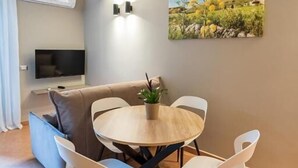 A dining area with a round table, four chairs, a sofa, a flat-screen TV, and a painting on the wall.