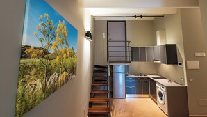 A compact kitchen with a washing machine, a small sink, and a staircase leading to a door.