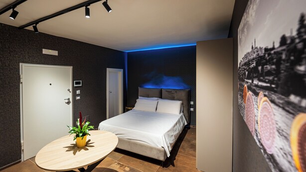 A modern hotel room with a bed, a round table with a plant, and a cityscape mural on the wall.