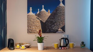 A wall-mounted painting of traditional architecture, a coffee maker, a potted plant, and a mug on a wooden table.