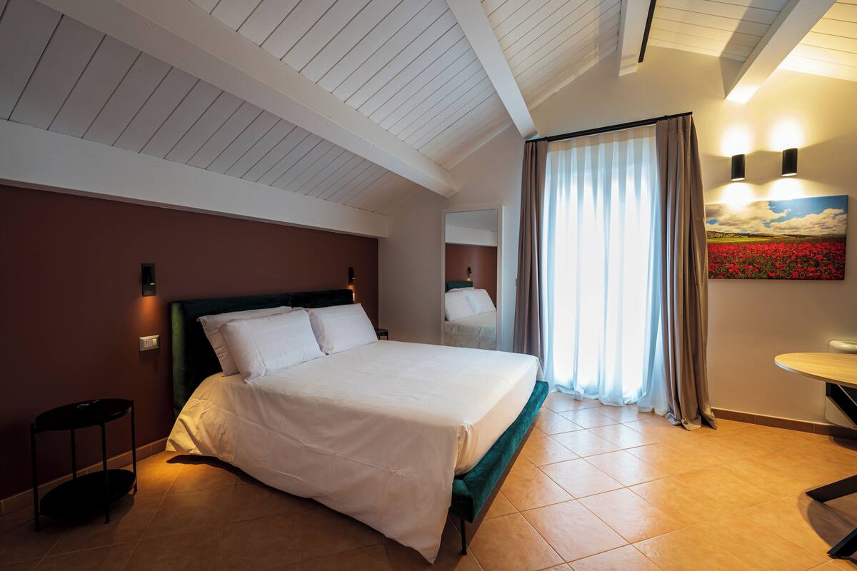 A hotel room with a bed, a nightstand, a table, and a painting on the wall.