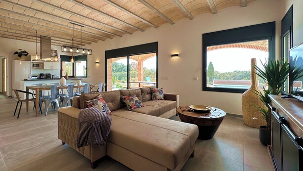 A spacious living area with a large L-shaped sofa, a dining table with chairs, a kitchen in the background, and large windows providing natural light. - The Private Accommodation Villa in Peralada (Peralada)