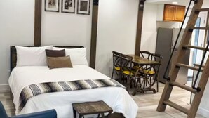 A bedroom with a bed, a small table, a chair, a wooden ladder, and a dining area with a table and chairs. - Perfect Studio - Walking distance of Lava Hot Springs Pools (Lava Hot Springs)