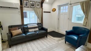 A living room with a black leather sofa, a blue armchair, a wooden table, and a large window with curtains. - Perfect Studio - Walking distance of Lava Hot Springs Pools (Lava Hot Springs)