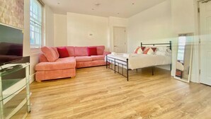 A spacious room with a large bed, a sofa, a TV, and a glass cabinet. - Essex Studio Retreat - Flat 4 (Chelmsford)