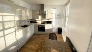 A modern kitchen with white cabinets, a built-in oven, and a window providing natural light. - Essex Studio Retreat - Flat 4 (Chelmsford)