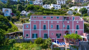 Un edificio rosa de varios pisos con balcones, una zona de piscina y un paisaje con colinas.