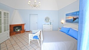 Un dormitorio con cama, tocador blanco, espejo, chimenea y un cuadro en la pared.