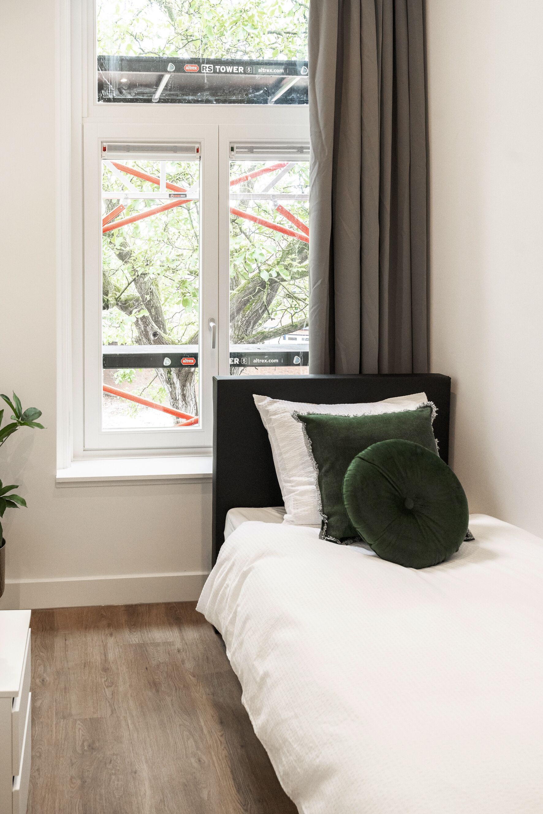 Een slaapkamer met een bed, een raam met uitzicht op bomen, en een gordijn.