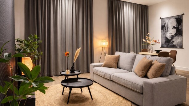 Ein modernes Wohnzimmer mit einem grauen Sofa, einem runden Couchtisch und einer Lampe.