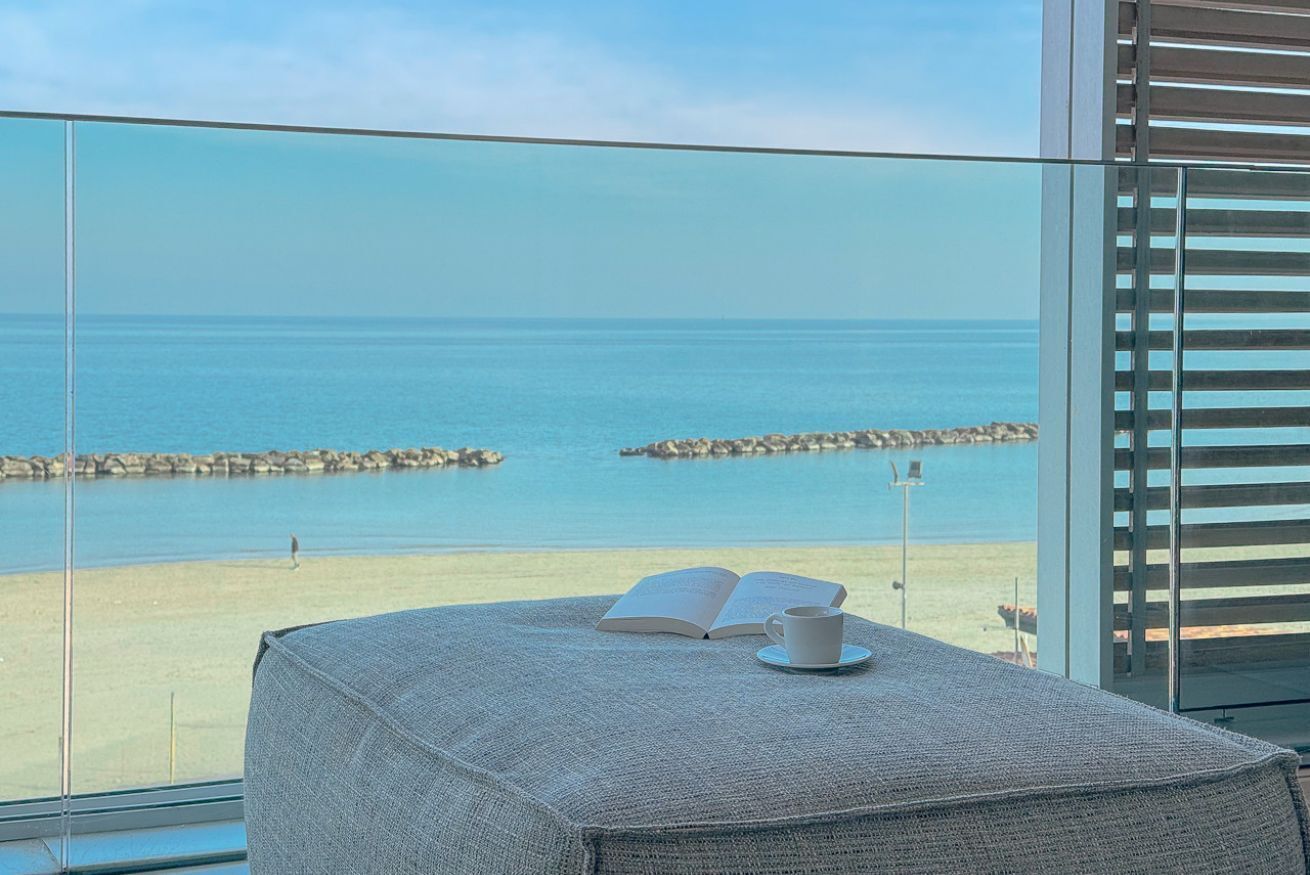 Un balcone con vista sul mare, un tavolo con un libro e una tazza, e una finestra con persiane.