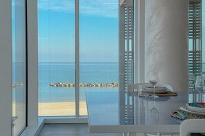 Zona pranzo con vista sul mare, un tavolo in vetro e una sedia bianca.