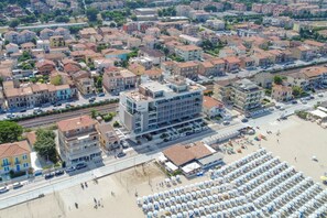 Vista aerea di una cittadina costiera con edifici residenziali, una spiaggia con ombrelloni e un binario ferroviario.
