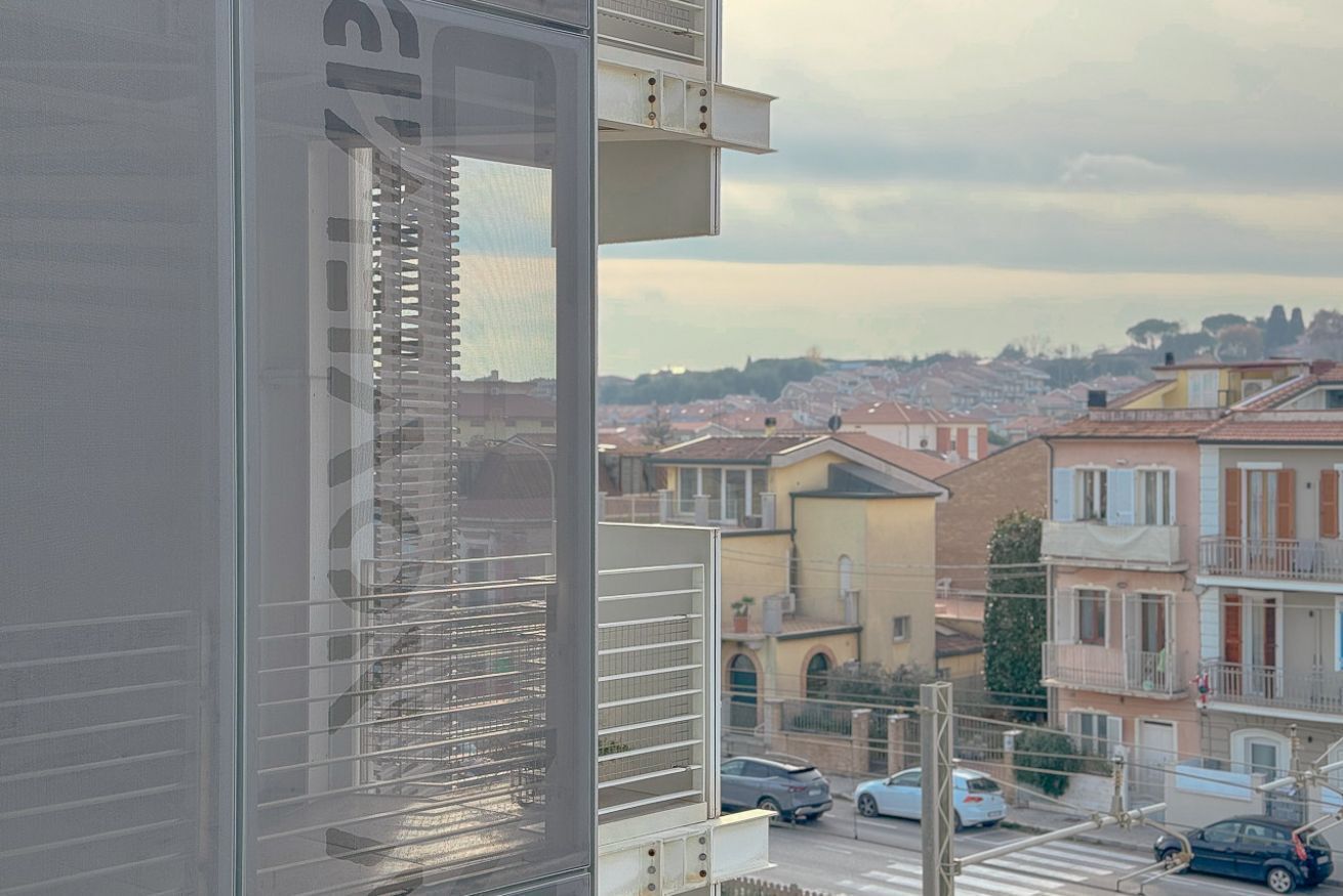A view from a window with blinds, overlooking a residential area with buildings and parked cars.