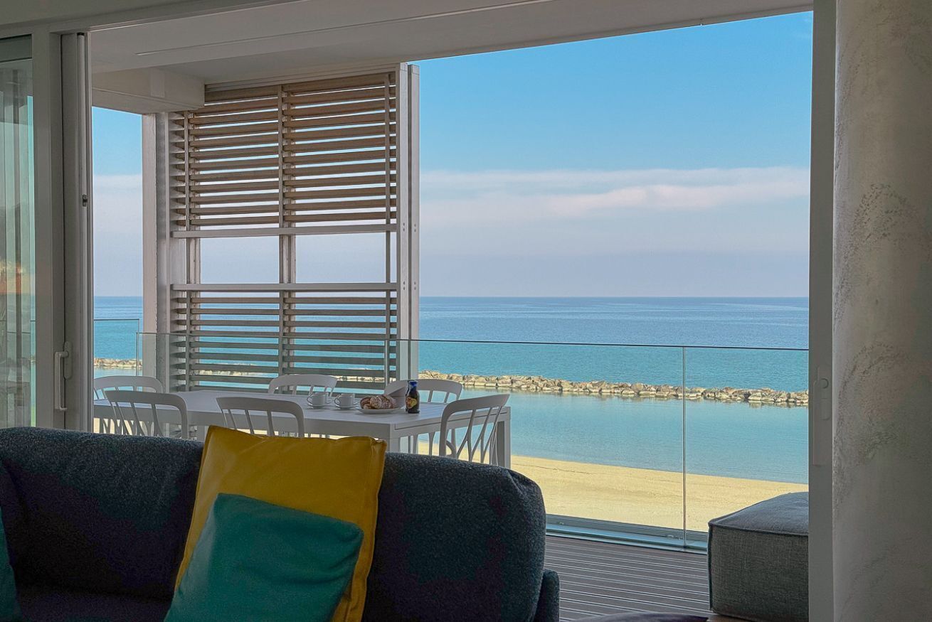 Un balcone con vista sul mare, un tavolo con sedie e un divano con cuscini.