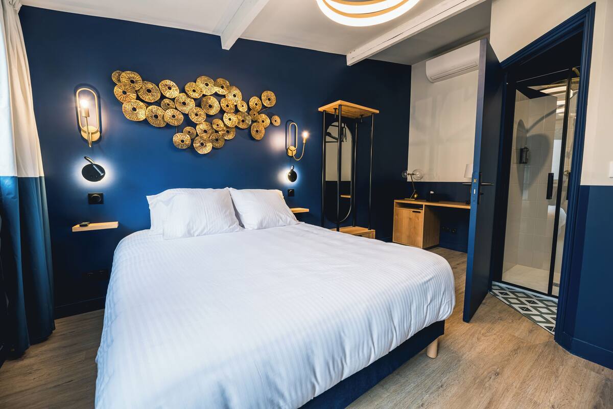 A modern bedroom with a large bed, a wall-mounted light fixture, and a mirror.